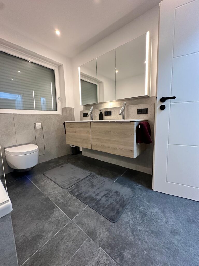Ein modernes, grau gefliestes Bad mit großem Spiegelschrank über dem Waschbecken